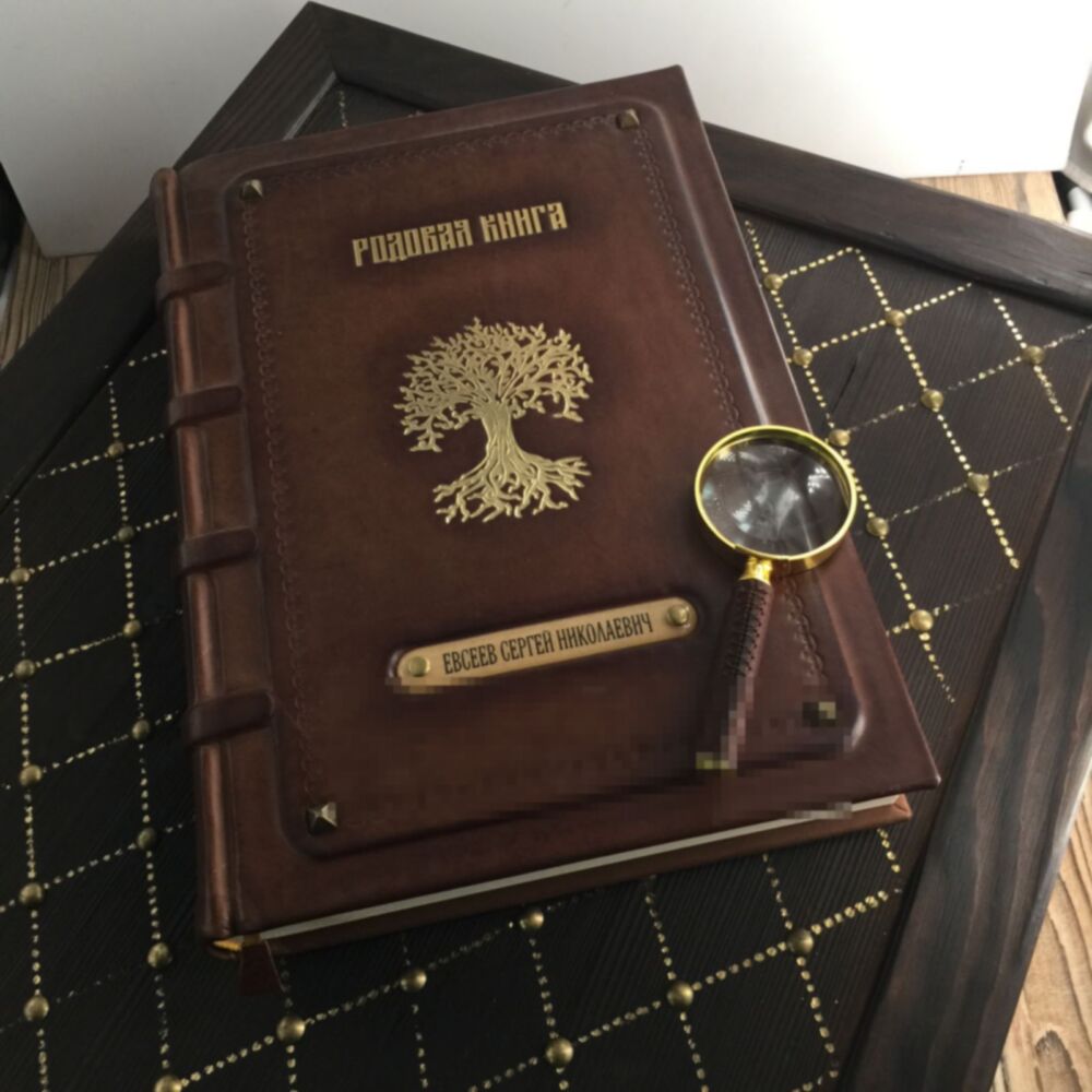 Кожаная родовая книга с тиснением родового древа золотой фольгой и латунной лупой лежит на фамильном сундуке