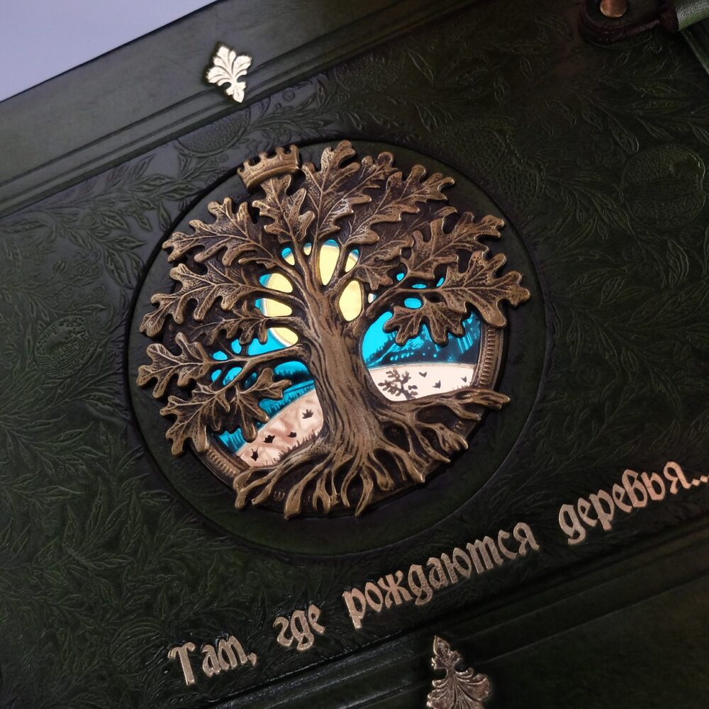 Тёмно-зелёная кожаная обложка с накладным древом и витражом, ниже тиснение «Там, где рождаются деревья…»
